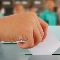 Mano de una persona estudiante votando en el aula