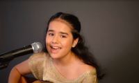 La ganadora canta delante de un micrófono y sostiene una guitarra.