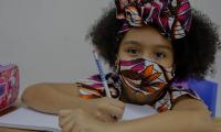Niña con vestimenta afrocostarricense recibe lecciones. Utiliza mascarilla.