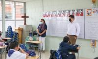 Presidente está frente a un grupo de estudiantes en un aula. Su maestra acompaña