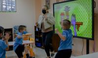 Maestras y niños bailan en una clase. Al fondo una pantalla.