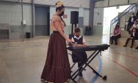 Mujer sostiene un micrófono y niña toca una pianola.