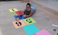 Mujer sonriente, acostada boca abajo pinta los números 5 y 6 en el piso