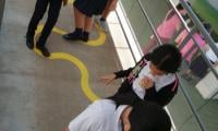 Estudiantes siguen una línea amarilla pintada en el piso que simula un camino