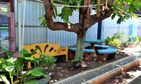 dos bancas de cemento de colores amarillo y verde, están debajo de un árbol.