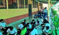 Niños sentados en el piso, juegan bingo con frijoles negros.