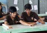 Dos persona jóvenes con uniforme en una mesa de trabajo, trabajando y revisando un plano